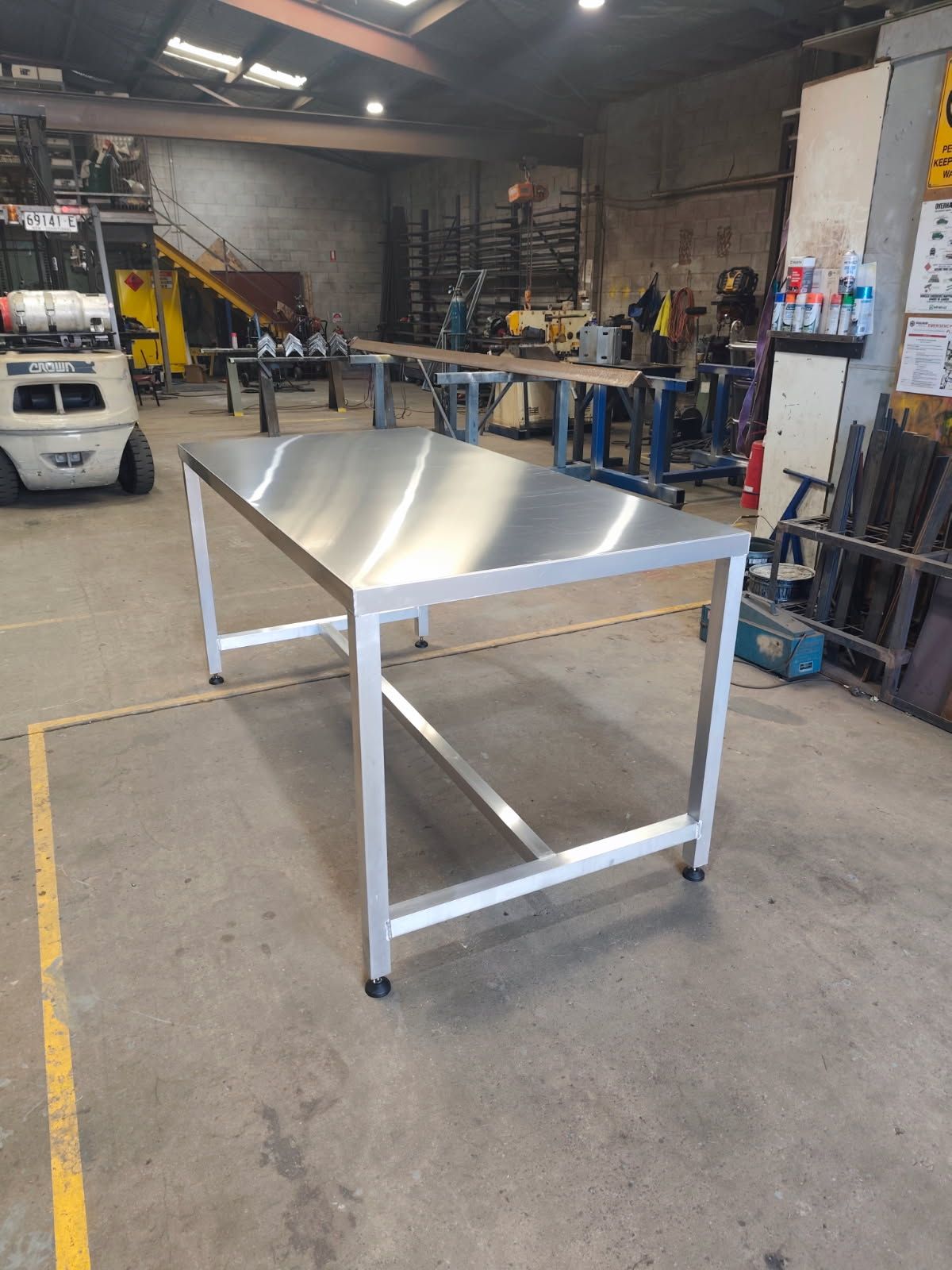 A rectangular stainless steel work table with a silver metal frame stands in the center of an industrial workshop — Highlander Metals in Kirrawee, NSW