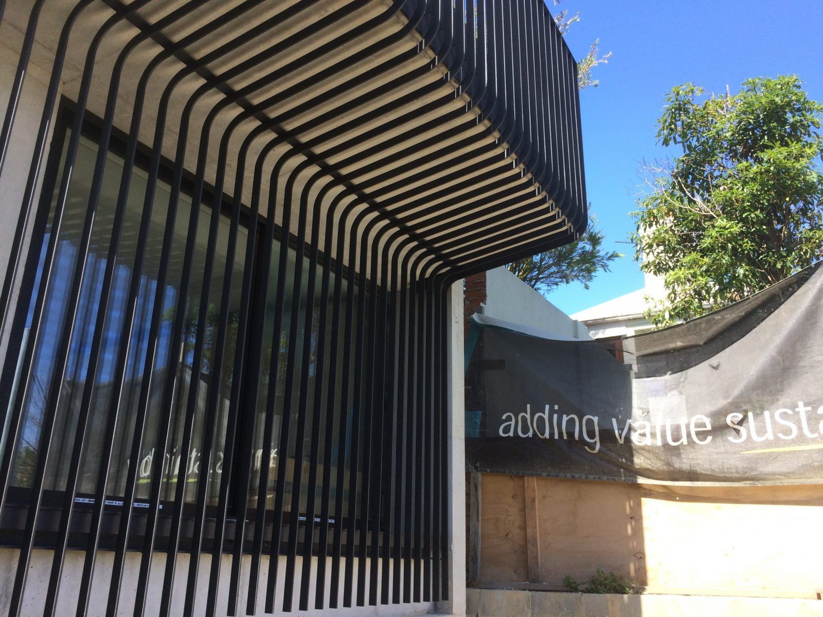 Black metal slats create a modern, curved canopy over a window, set against a bright blue sky and nearby construction — Highlander Metals in Kirrawee, NSW