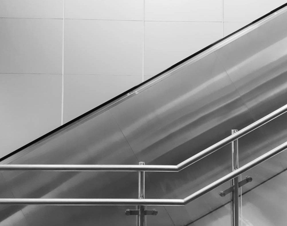 Black and White Image of an Escalator With Steel Handrails Against a Tiled Wall — Highlander Metals in Kirrawee, NSW