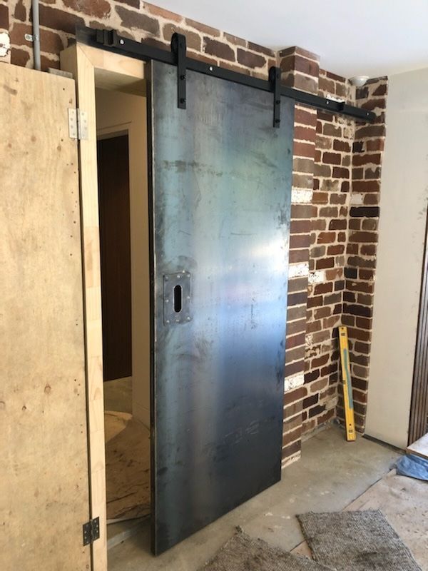 A modern steel sliding barn door installed against a rustic brick wall in an unfinished room — Highlander Metals in Kirrawee, NSW