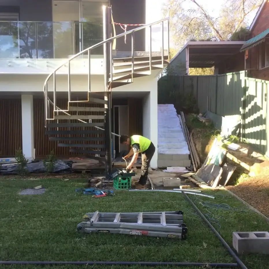 A Person in a Safety Vest Works Outside Near a Spiral Staircase and a Grassy Yard — Highlander Metals in Kirrawee, NSW