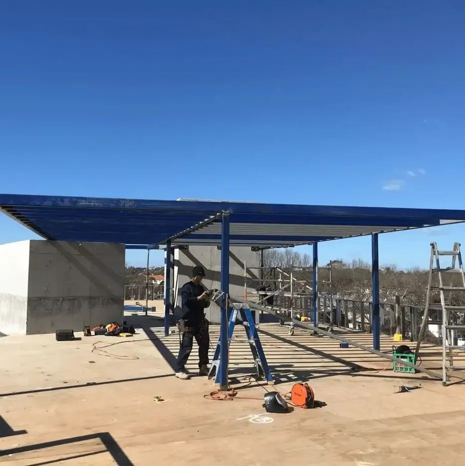 Man Installing a Blue-roofed Structure on a Rooftop Under a Clear Sky — Highlander Metals in Kirrawee, NSW
