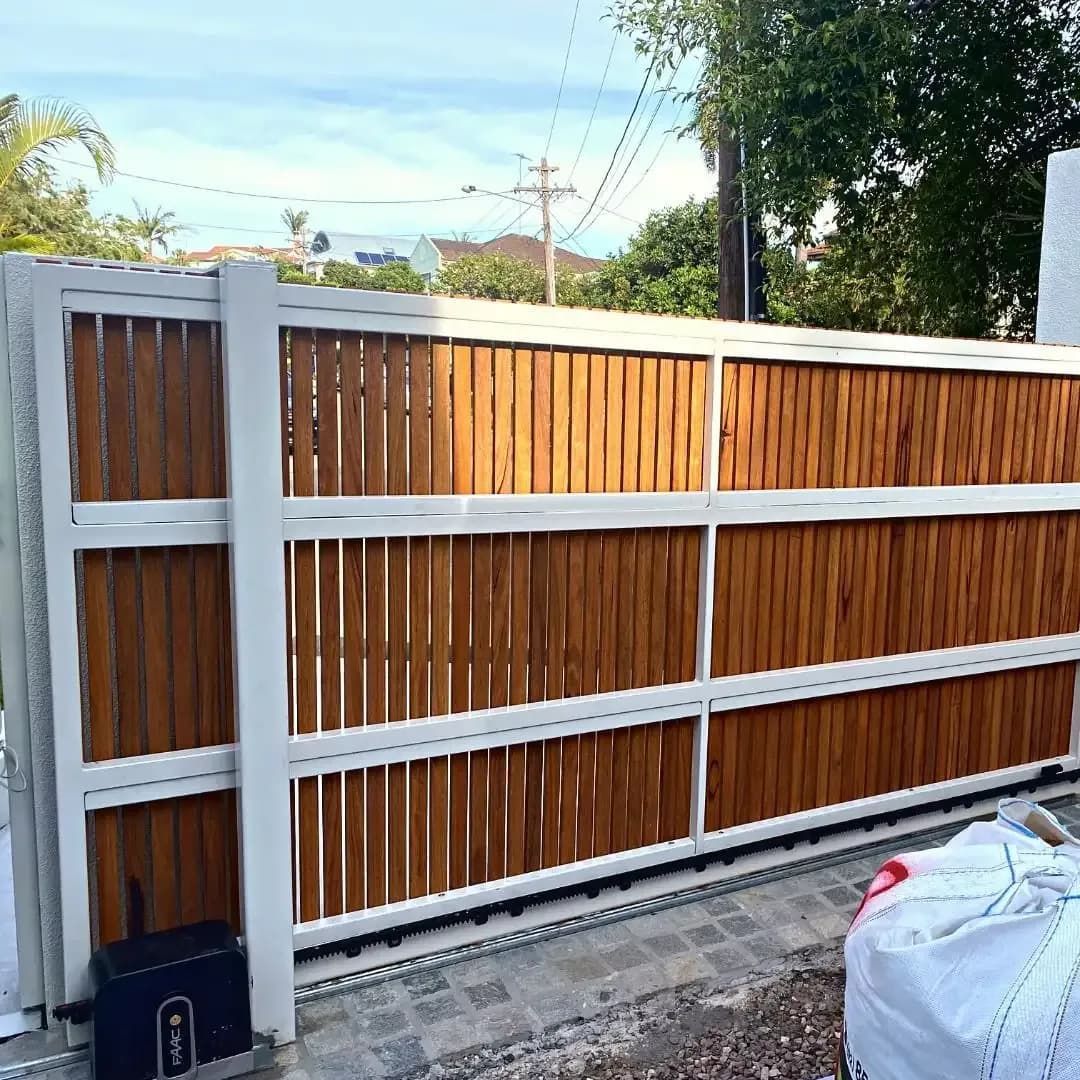 A sliding gate with a white frame and vertical brown wooden slats installed on a paved driveway — Highlander Metals in Kirrawee, NSW