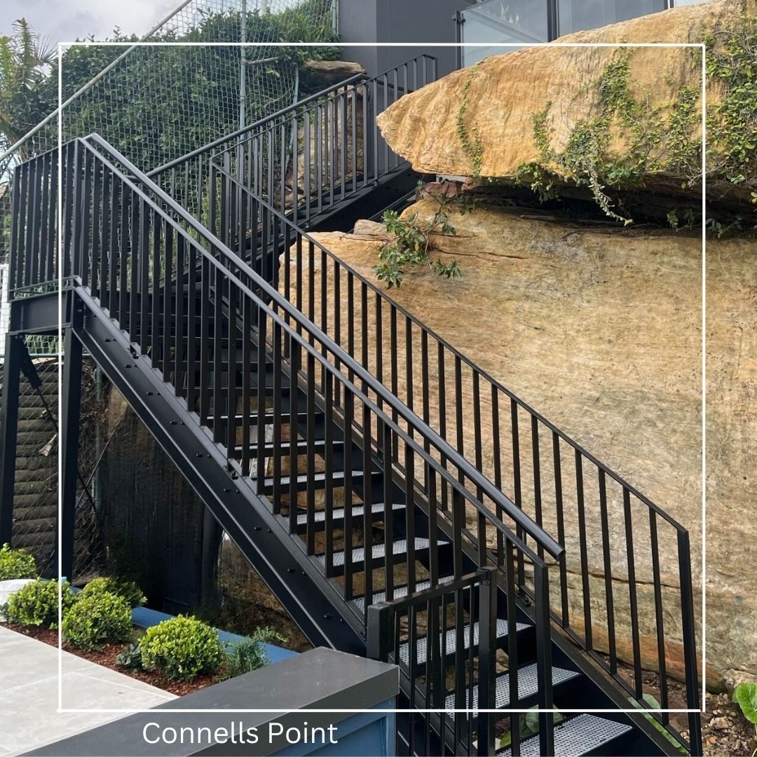 A black metal staircase with handrails built alongside a large natural sandstone rock face at Connells Point — Highlander Metals in Kirrawee, NSW