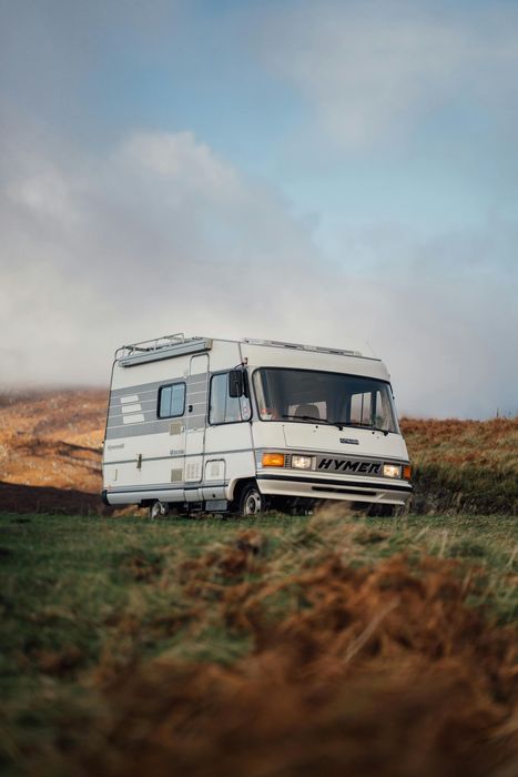 Weathered white RV parked in a grassy field under a cloudy sky.