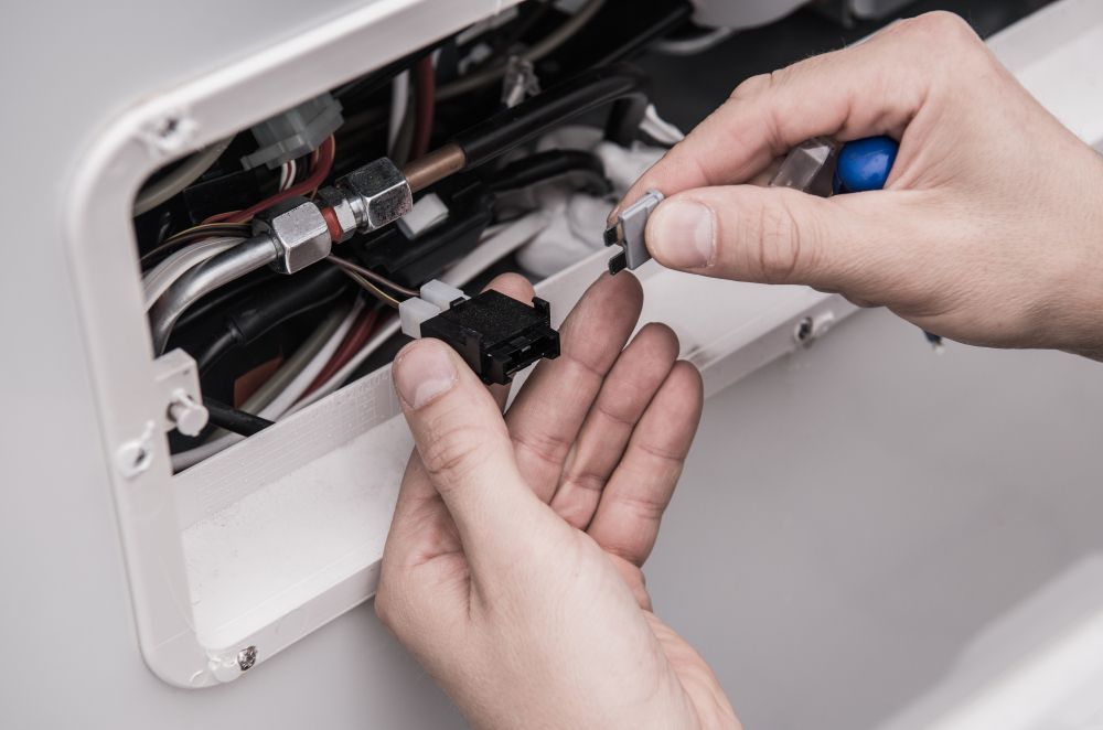 Hands using pliers to work on exposed electrical wiring inside a wall opening