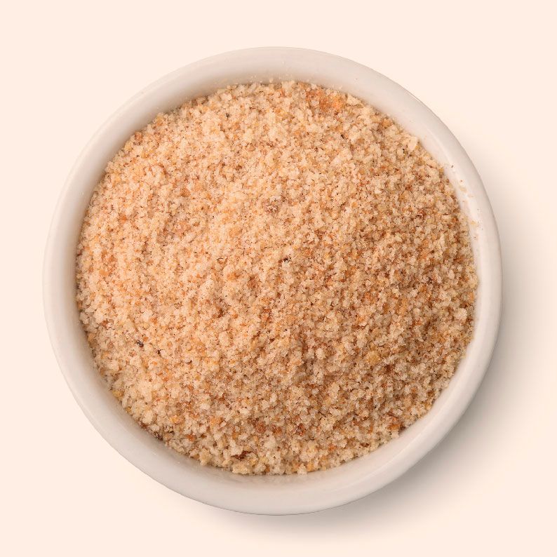 Un recipiente blanco lleno de migas de pan sobre un fondo blanco.