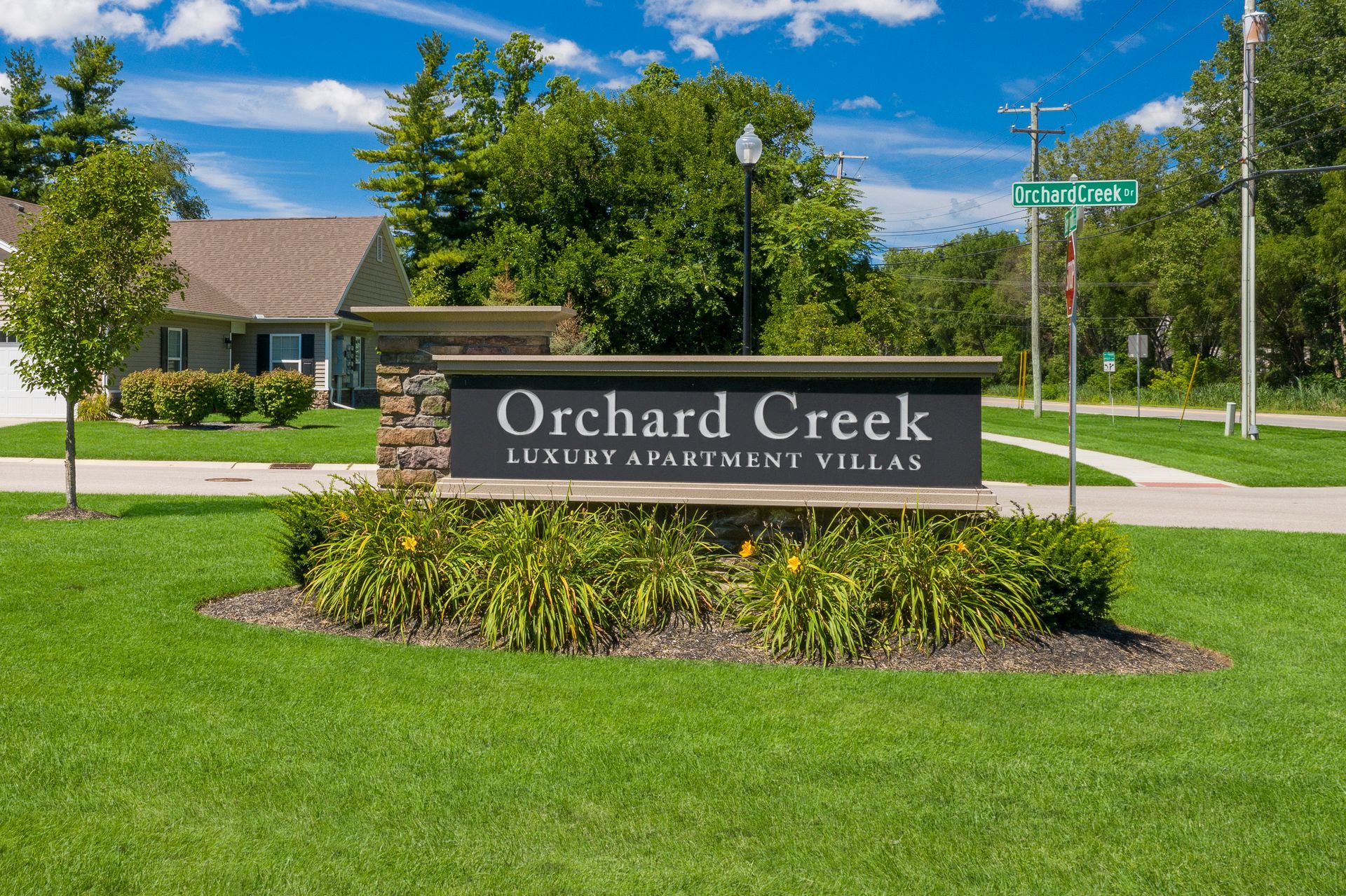 Sign for Orchard Creek luxury apartments/villas on a grassy lawn under a bright blue sky.
