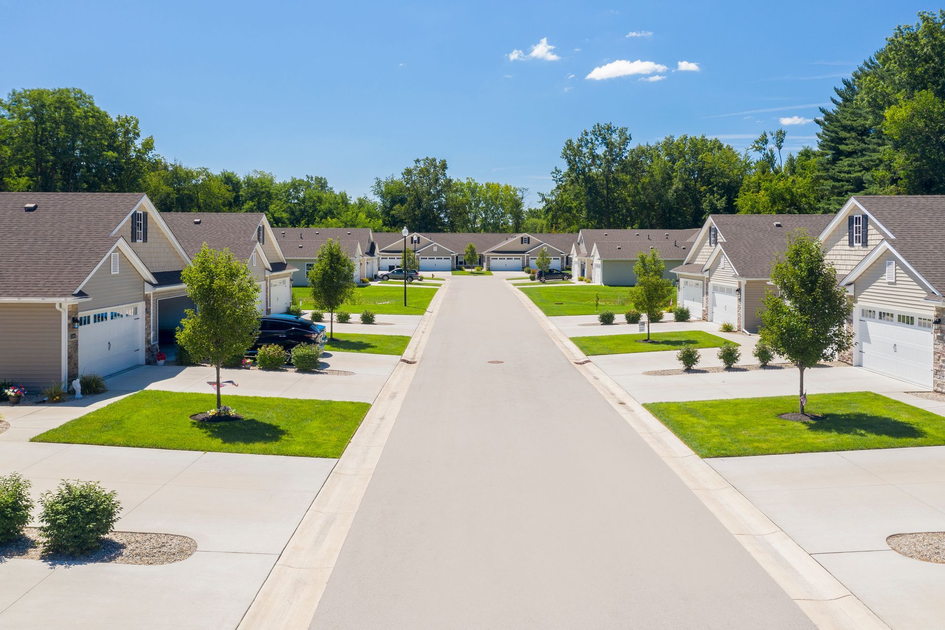 A suburban street with multiple houses, garages, and trees under a clear blue sky.