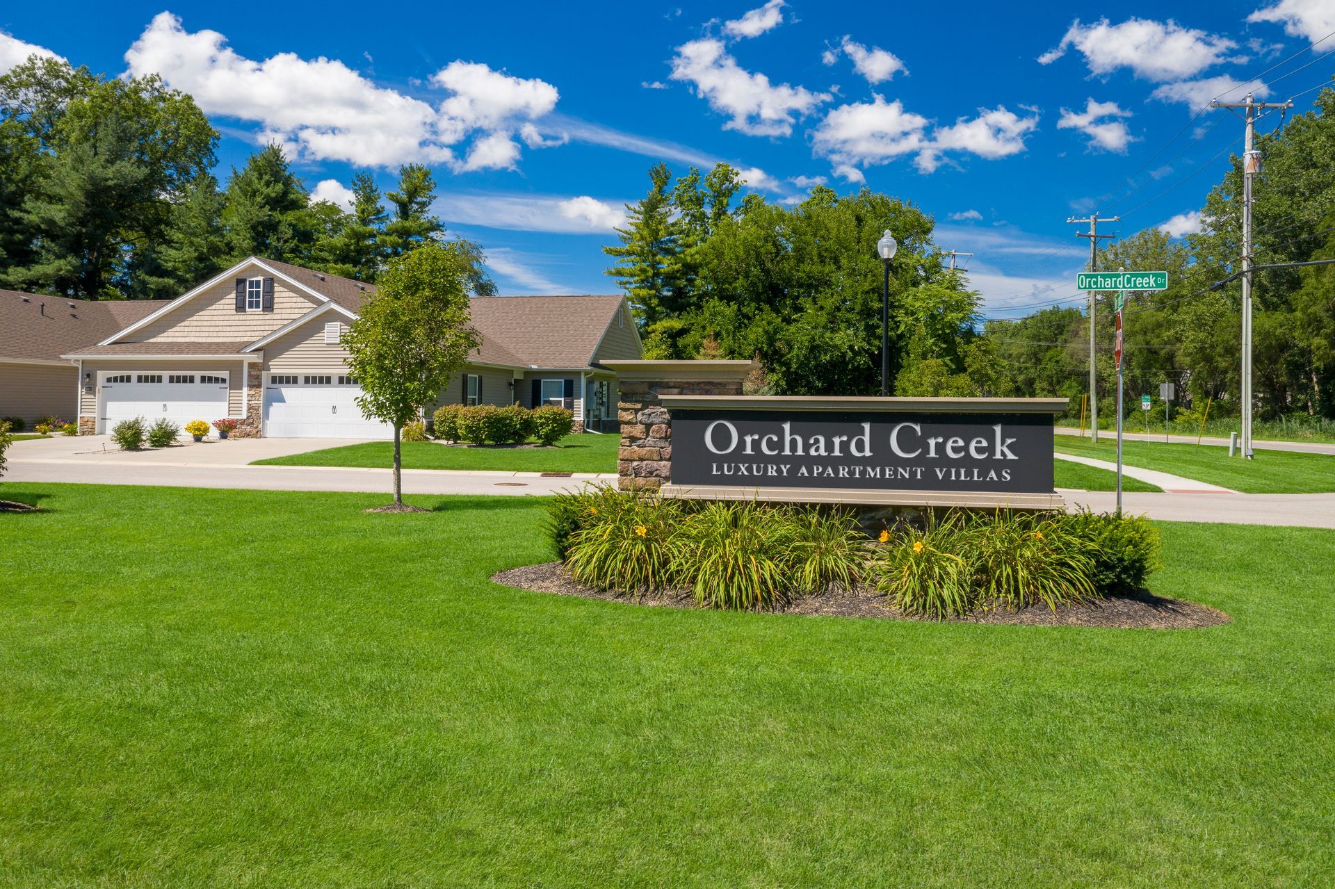 Orchard Creek apartment complex sign with green lawn, blue sky, and buildings in the background.