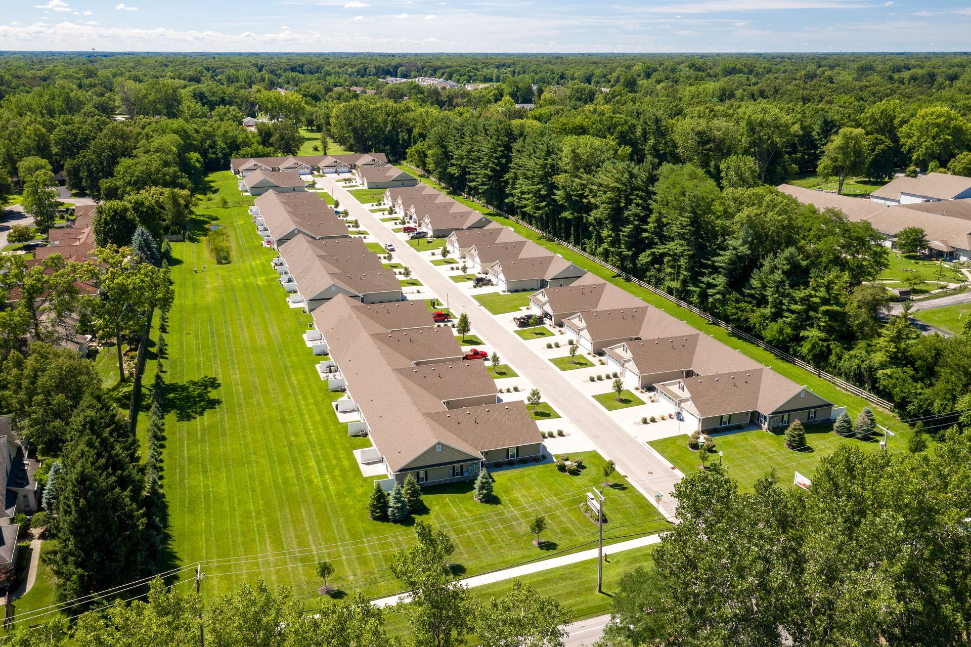 Aerial view of townhouses with brown roofs and white siding, surrounded by green lawns and trees.