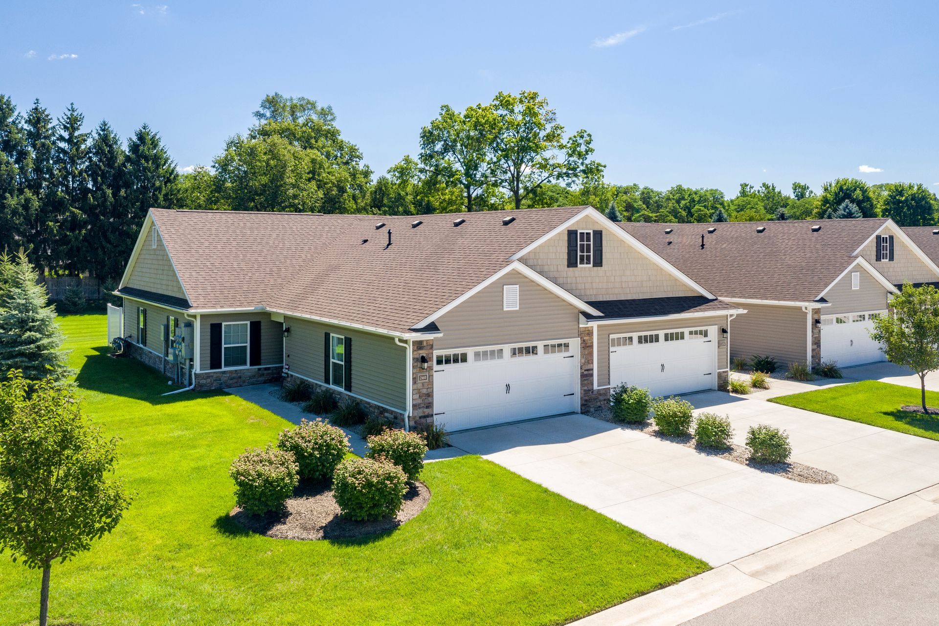 Suburban homes with garages, green lawns, and blue sky.