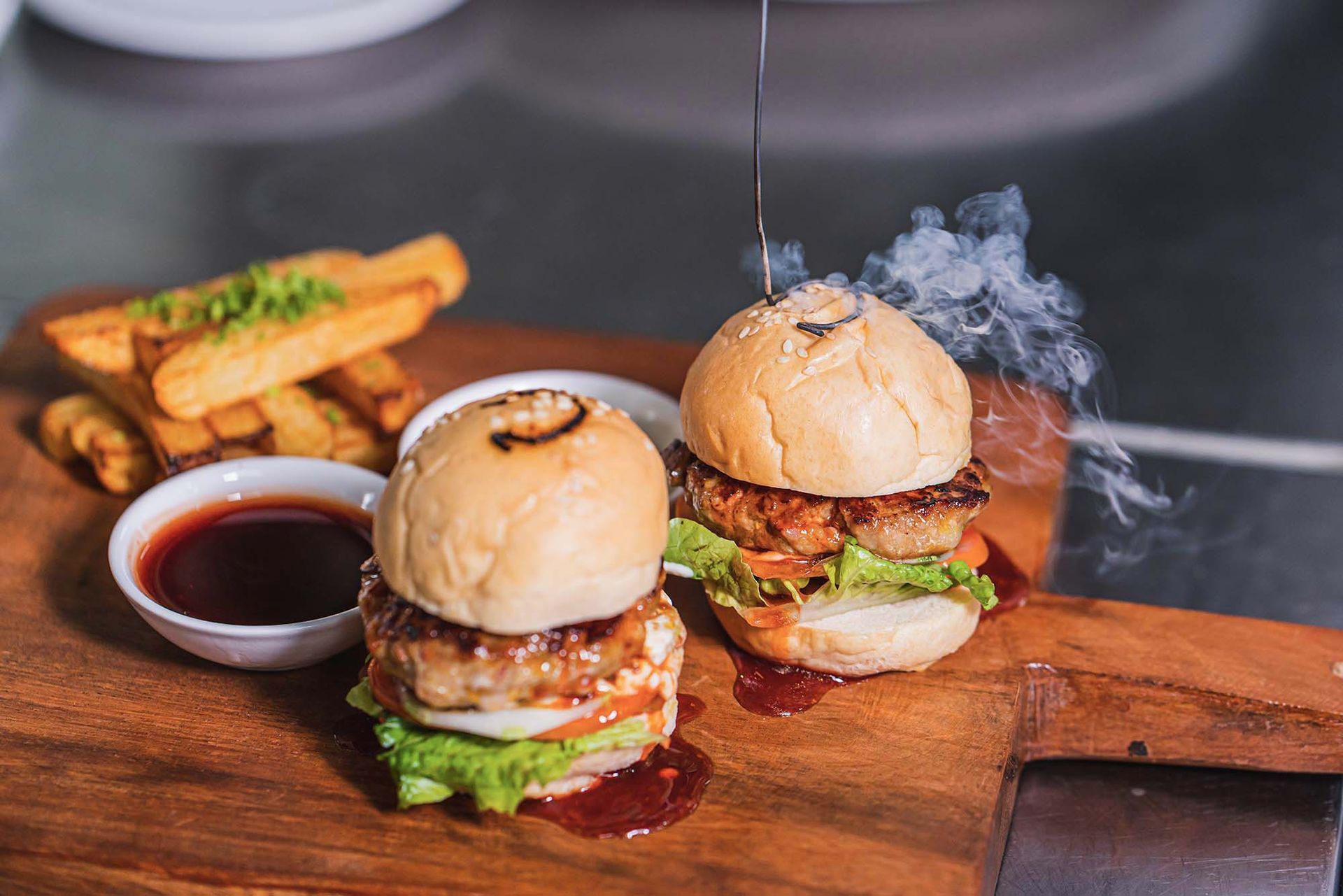 Two hamburgers and french fries on a wooden cutting board.