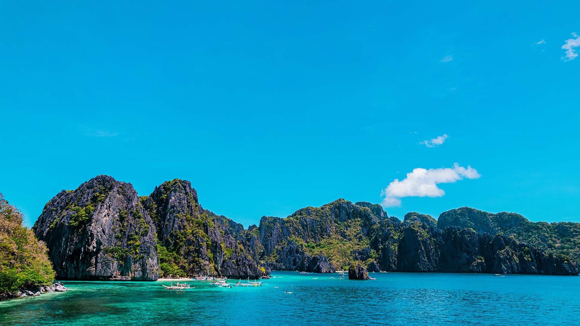 Turquoise lagoon with limestone cliffs and boats in El Nido, Palawan