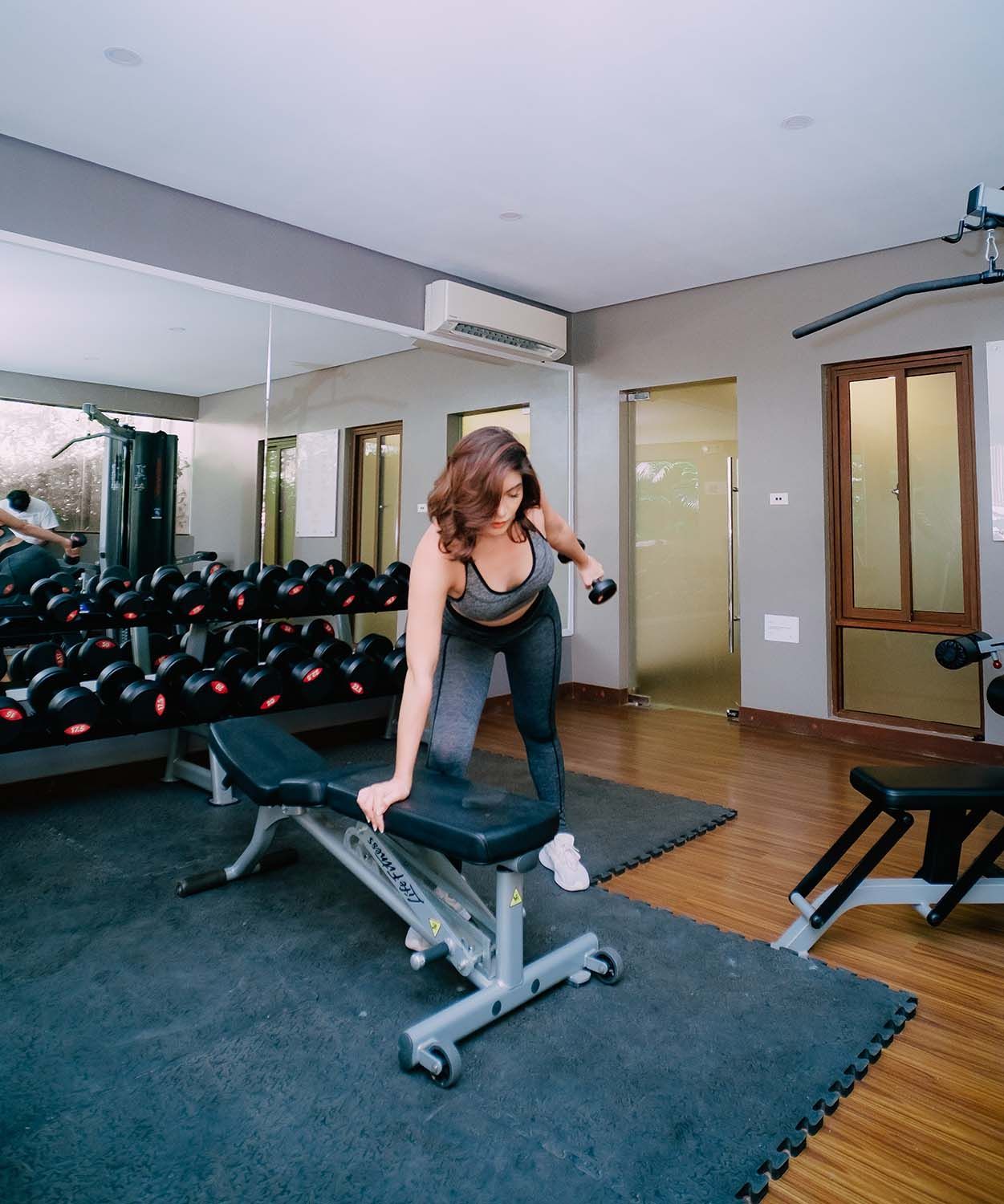 Woman working out with a dumbbell on a weight bench in a gym.