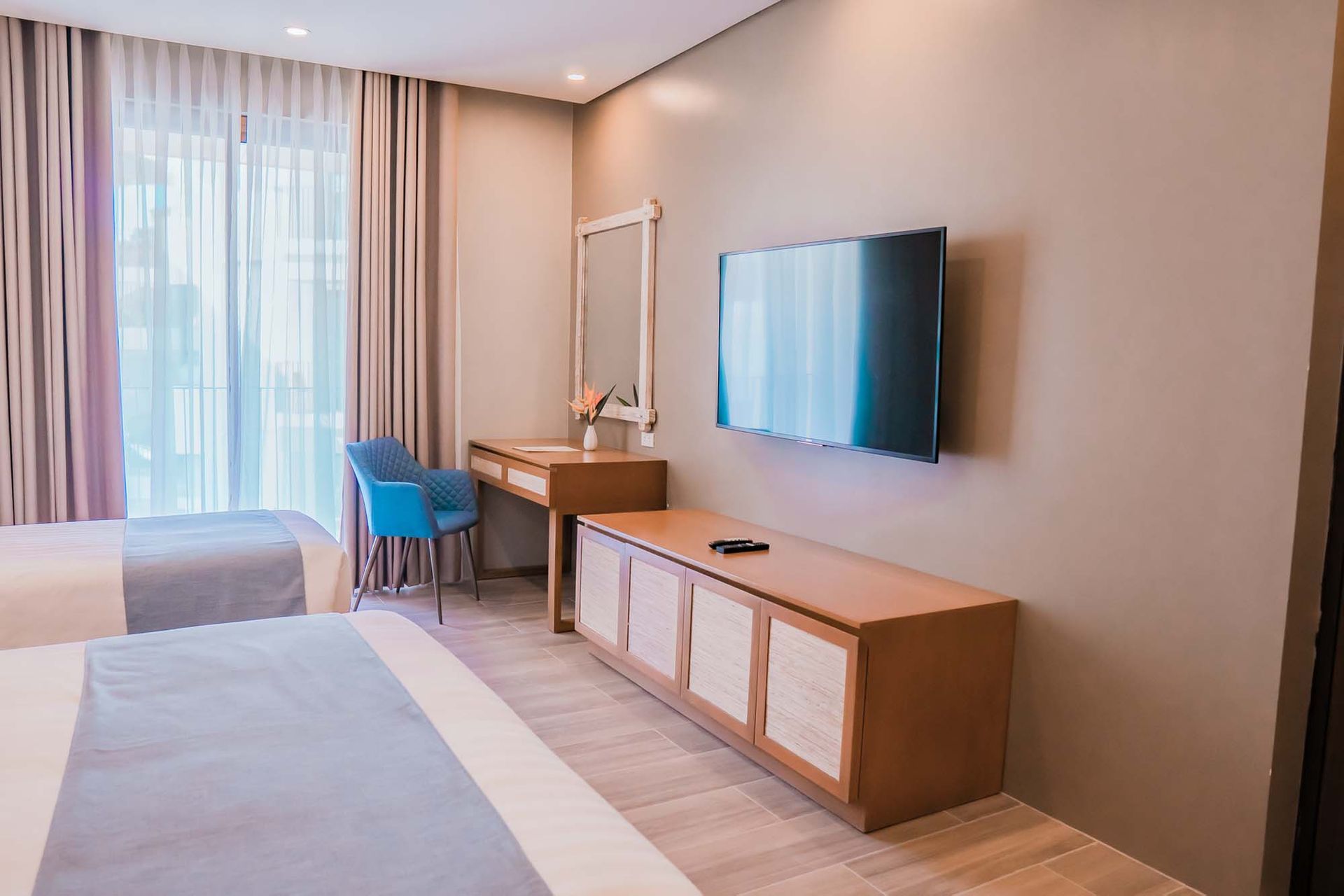 Family room with wooden TV console, vanity area with mirror, blue accent chair and partial view of a bed