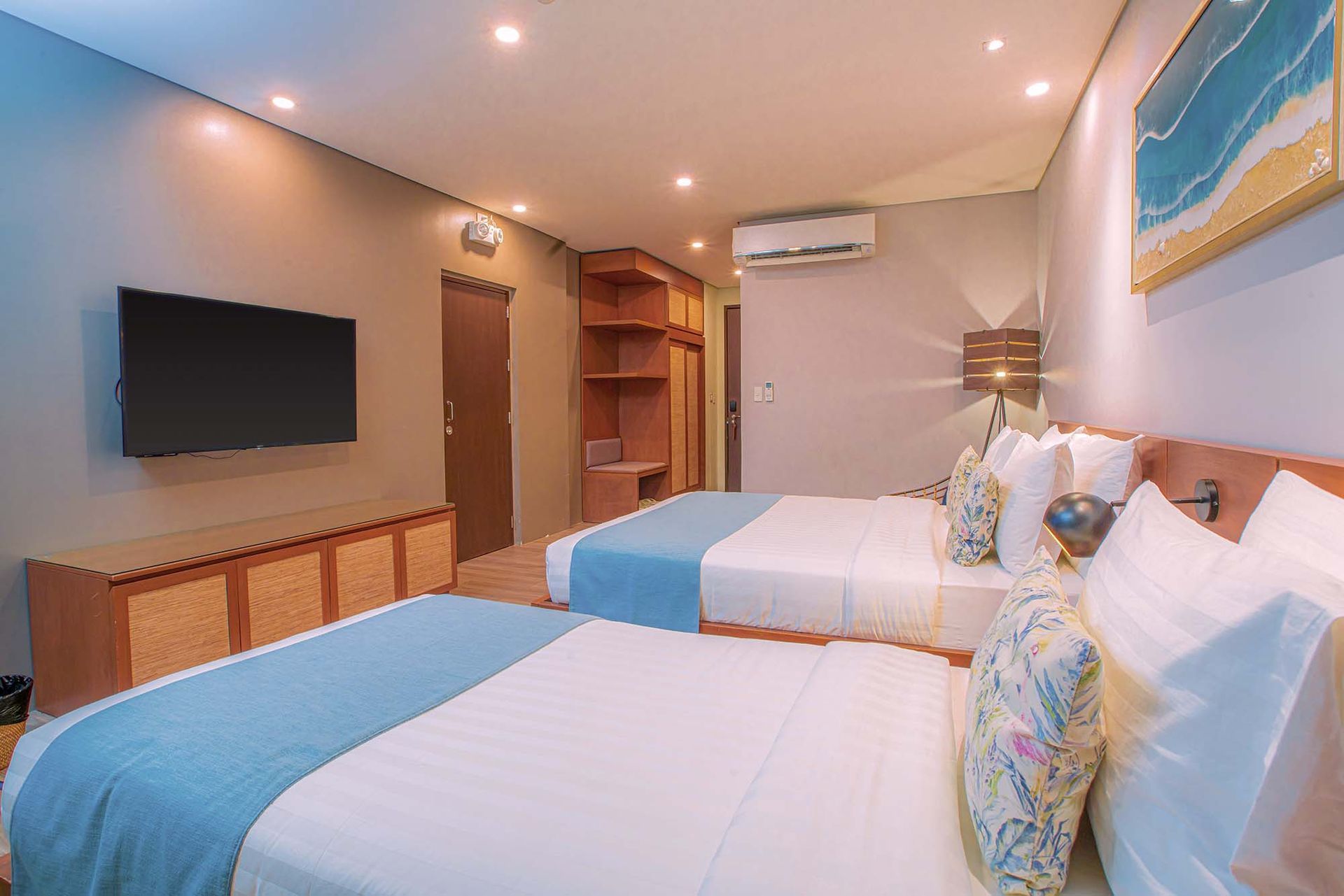 Twin bedroom with blue runners, floral cushions, wall-mounted TV and air conditioning unit