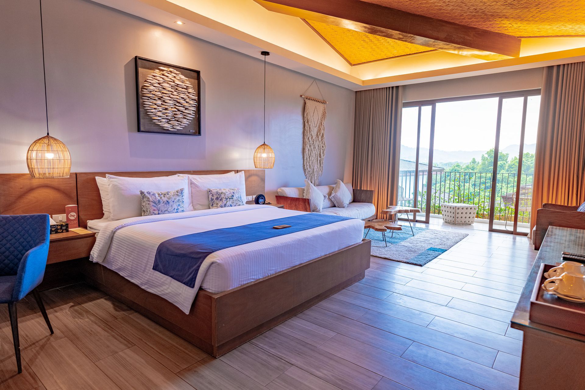 Bedroom with wooden furniture, bed with blue accents, and a lounge chair near a window.