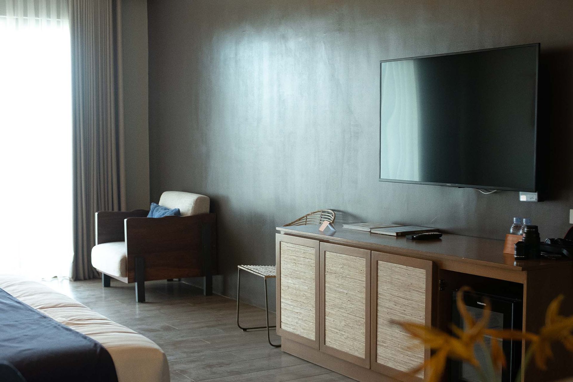 Living area with wall-mounted TV, comfortable seating, and wooden storage cabinet with woven panel details