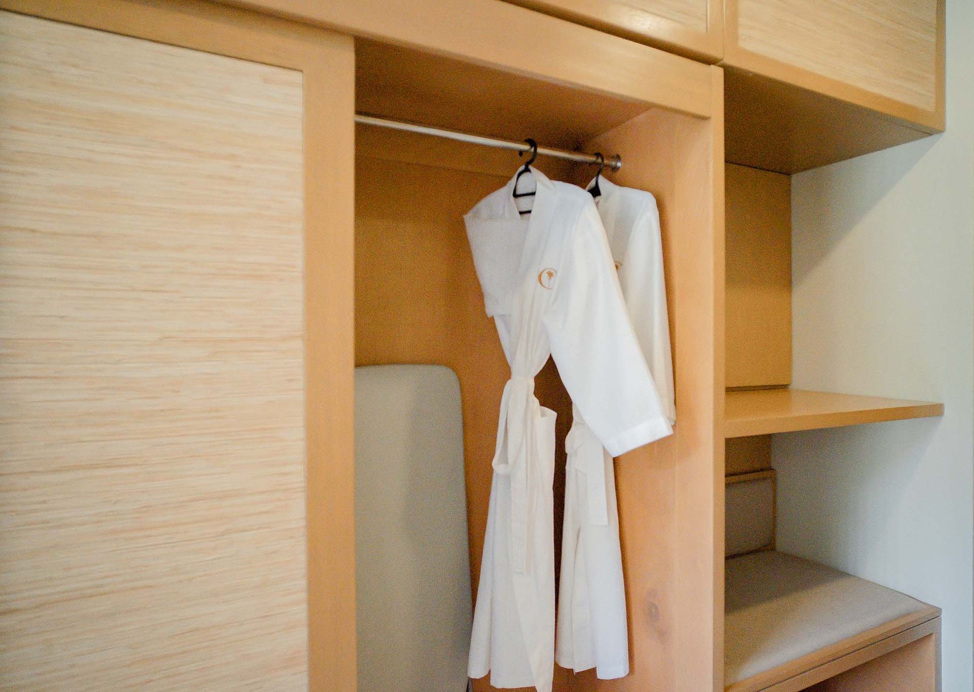 Built-in closet with wooden shelving and a plush white bathrobe with embroidered logo hanging on rod