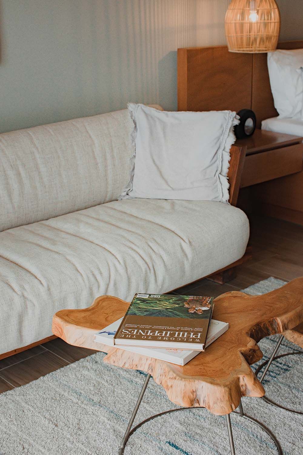 A white couch is sitting next to a wooden table with books in a hotel room in palawan
