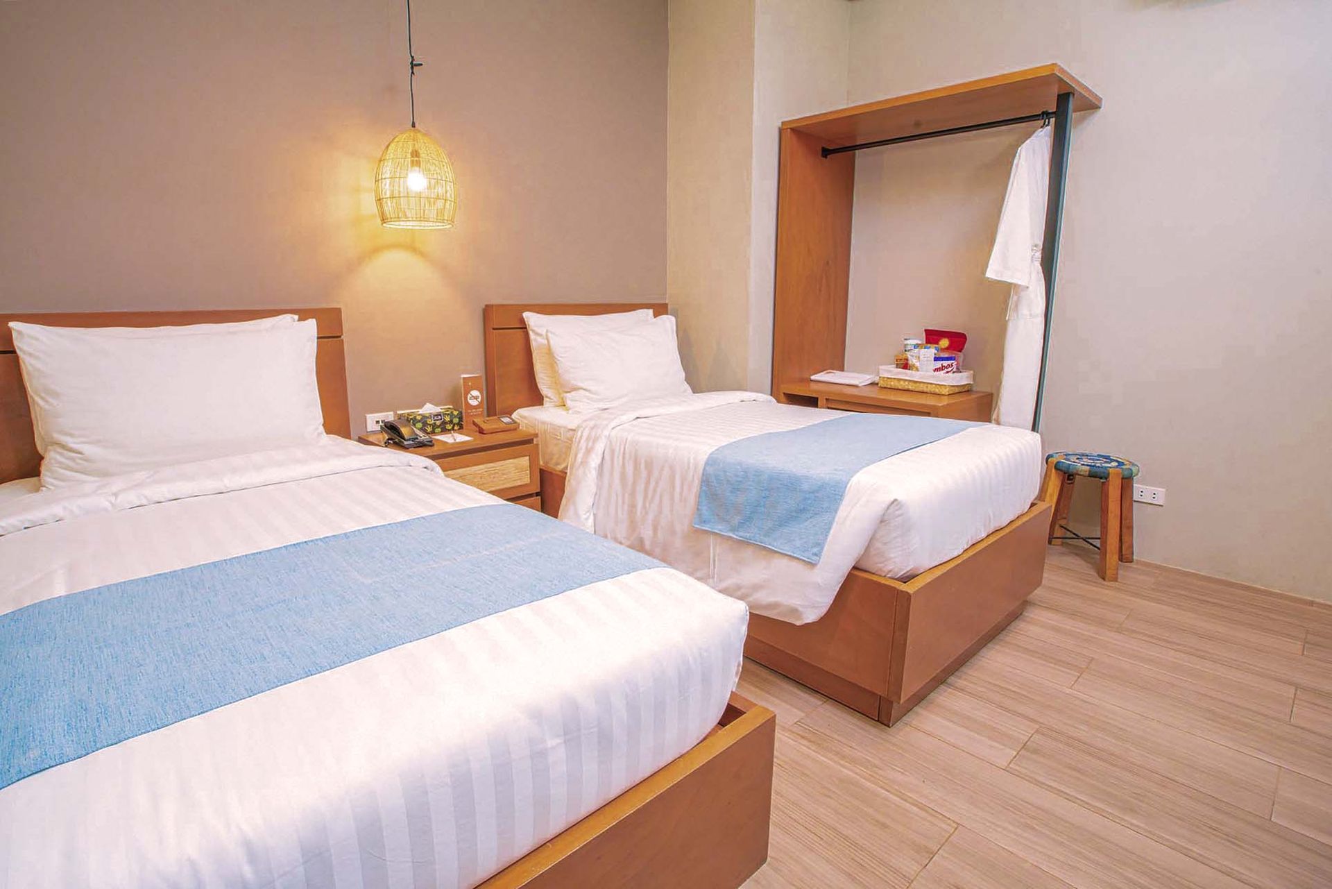 Twin beds with crisp white linens and light blue runners, pendant light, and wooden furniture