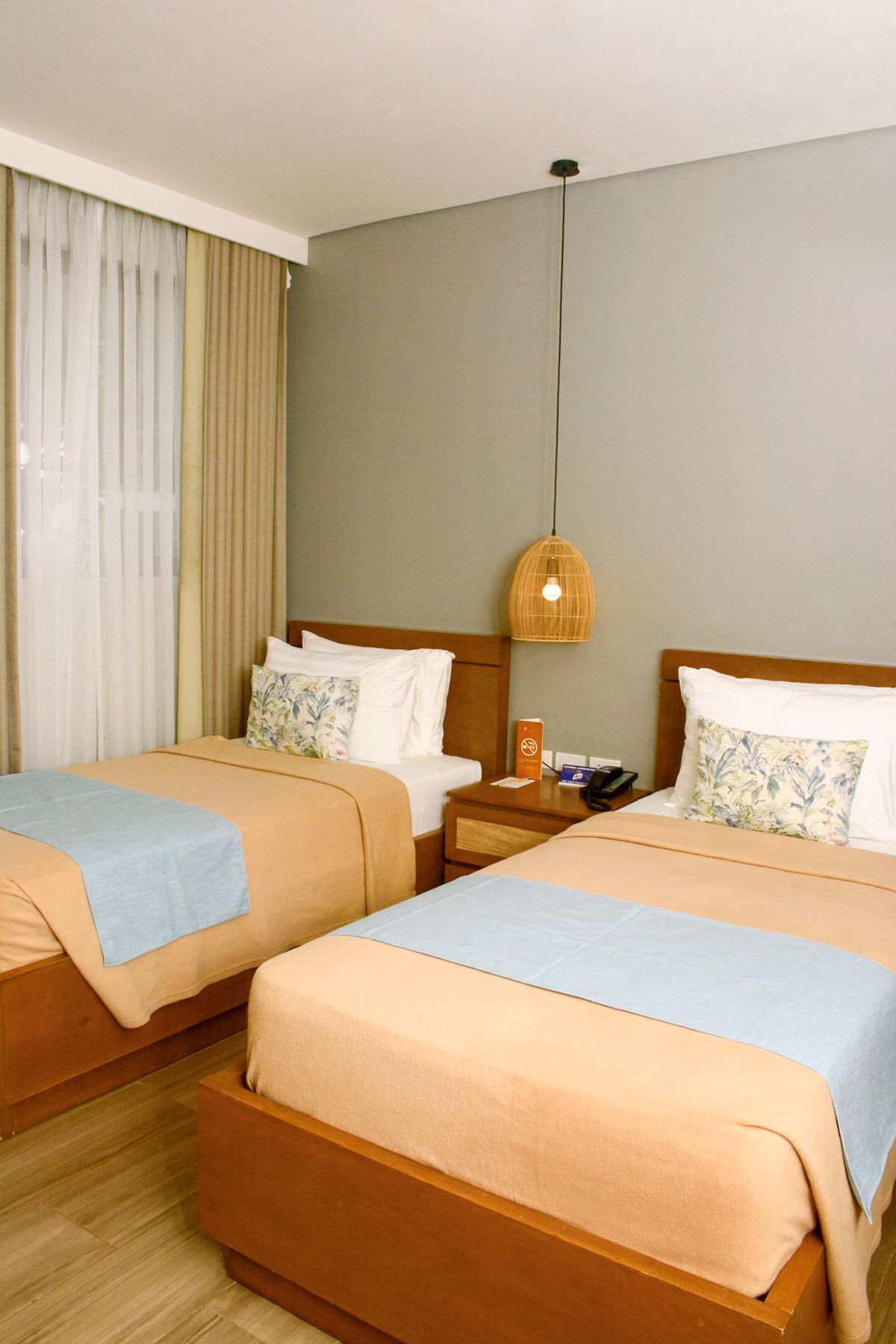 Cozy twin bedroom with beige and blue bedding, wicker pendant light, and floral pillows