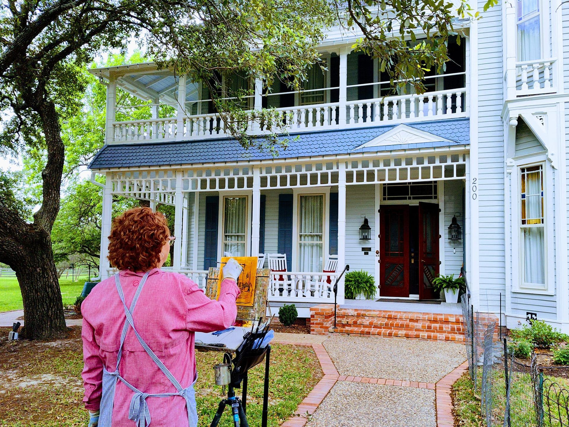 A woman in a pink apron is painting a picture of a house.