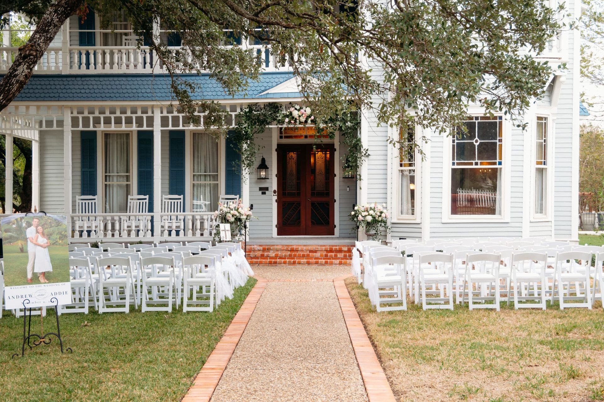 A white house with blue shutters and white chairs set up for a wedding ceremony.