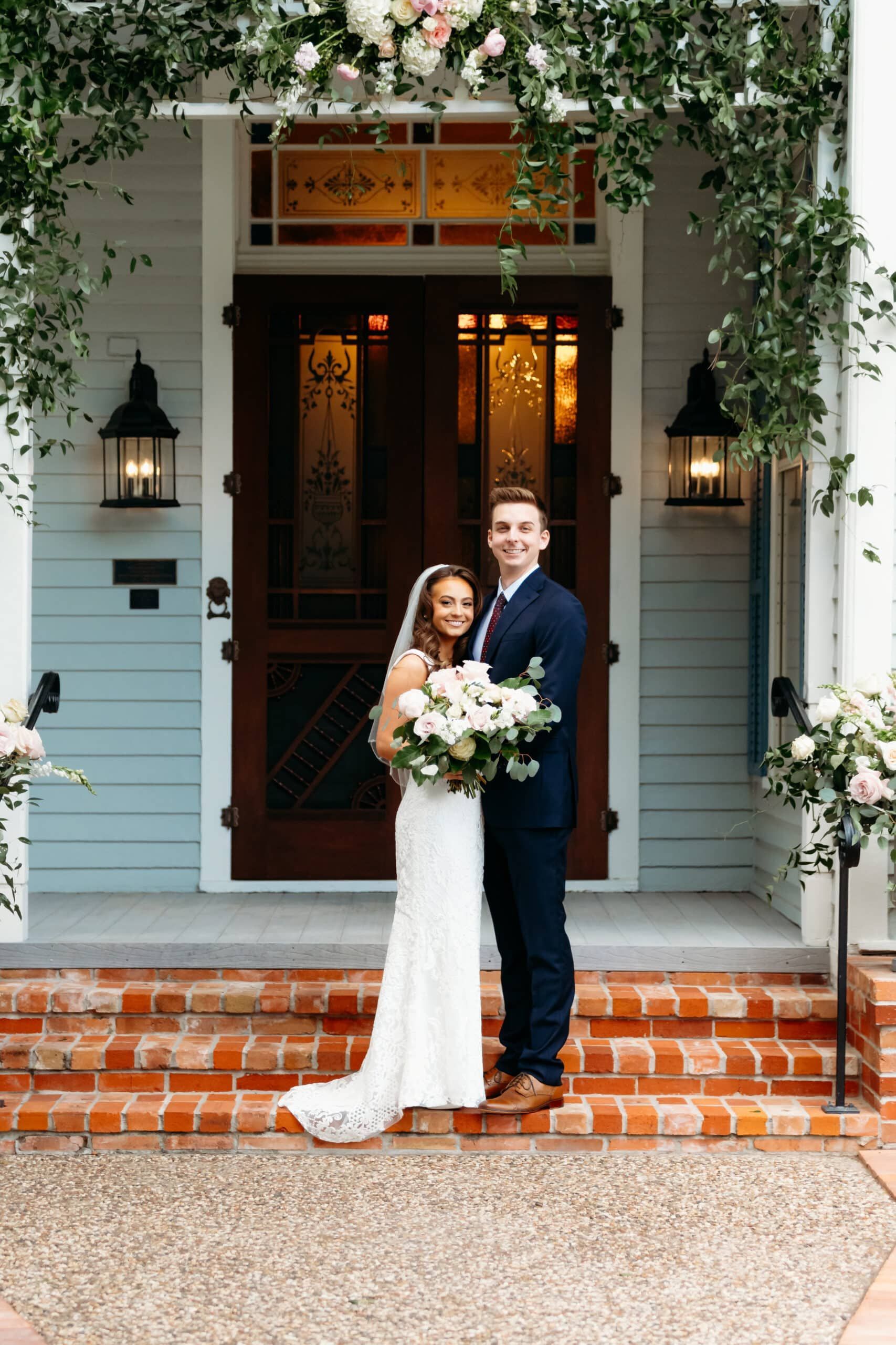 A bride and groom are posing for a picture in front of a house.
