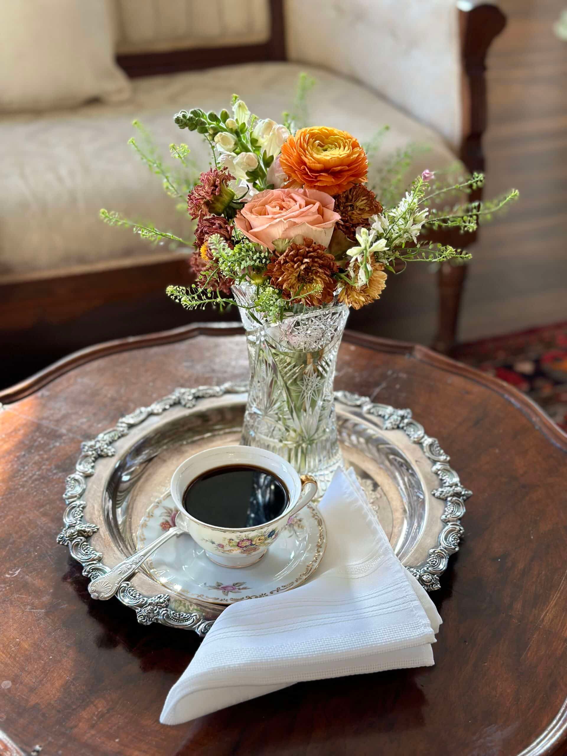 A cup of coffee and a vase of flowers on a tray on a table.