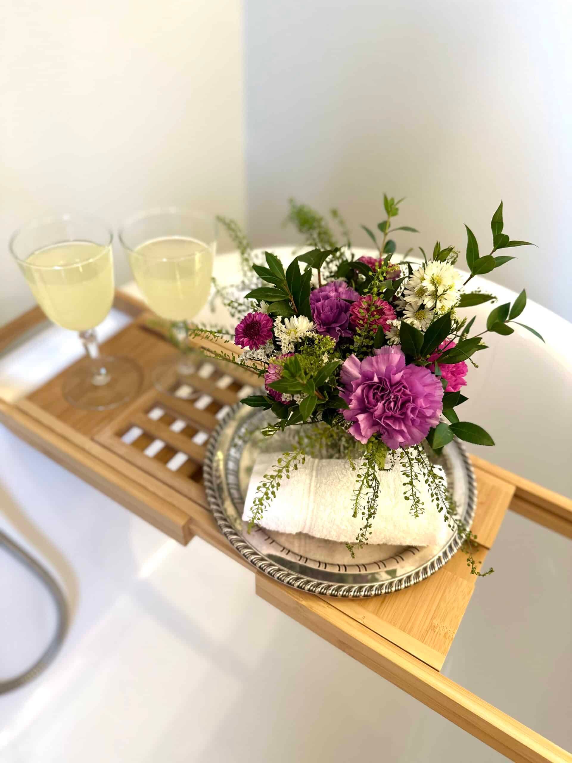 A wooden bathtub tray with flowers and wine glasses on it.