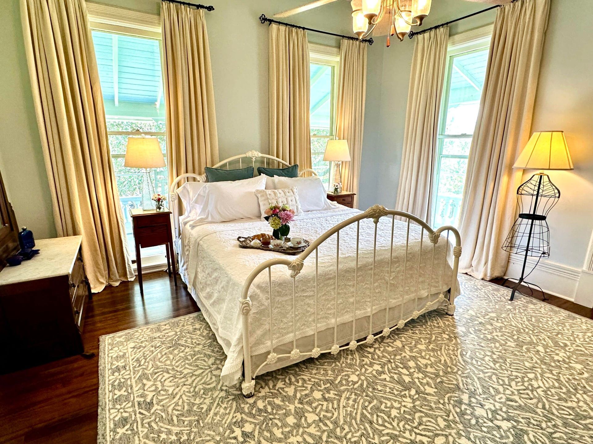 A bedroom with a large bed , two nightstands , a rug , and a chandelier.