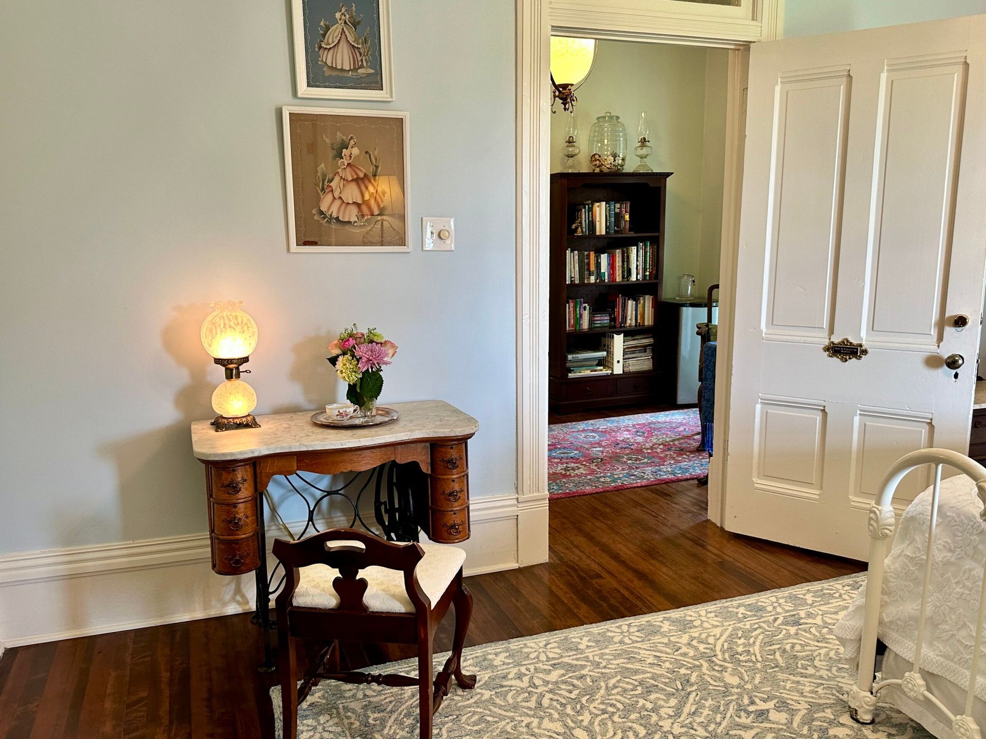 A bedroom with a desk , chair , lamp and bookshelf.