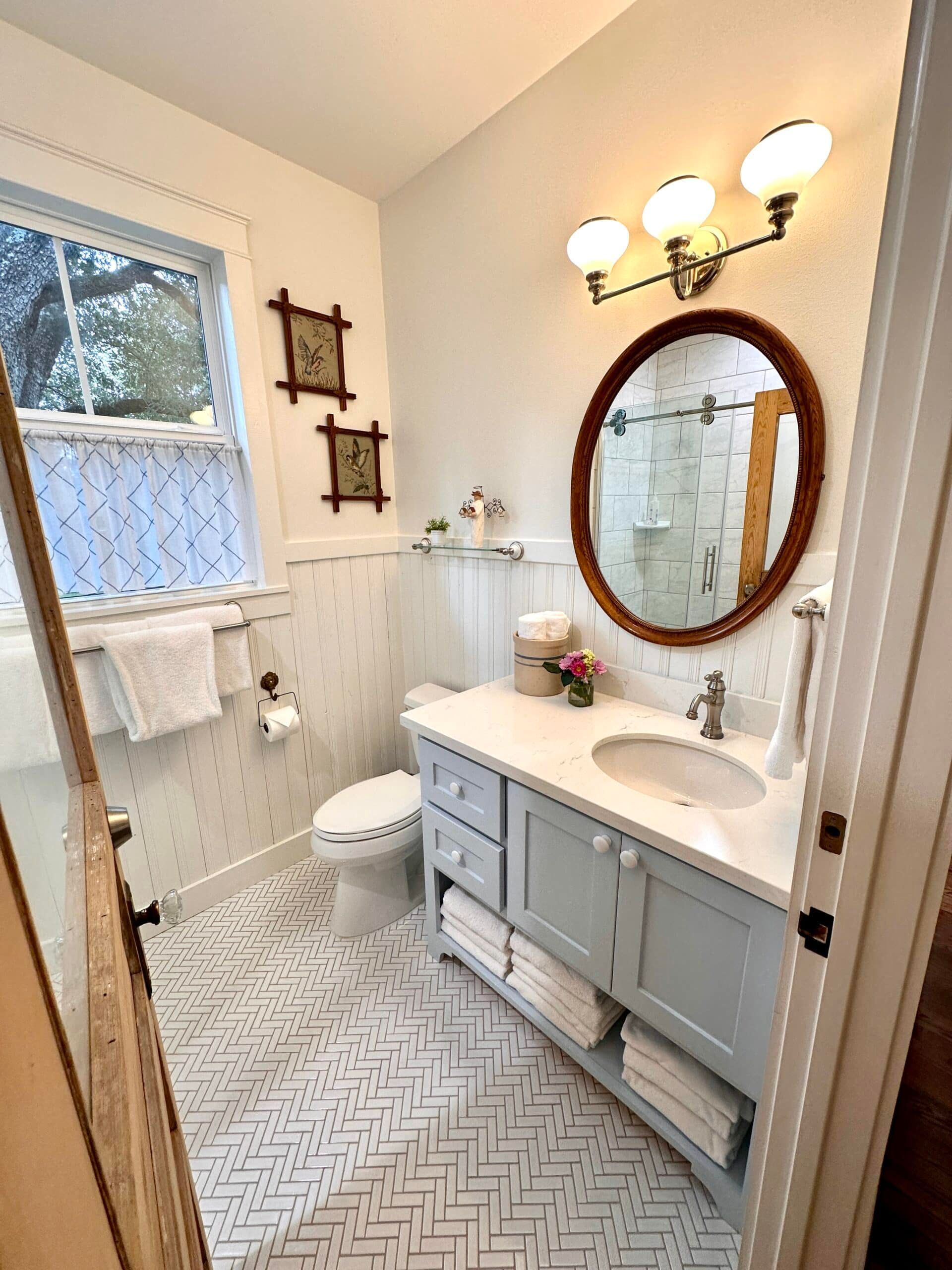 A bathroom with a toilet , sink , mirror and window.