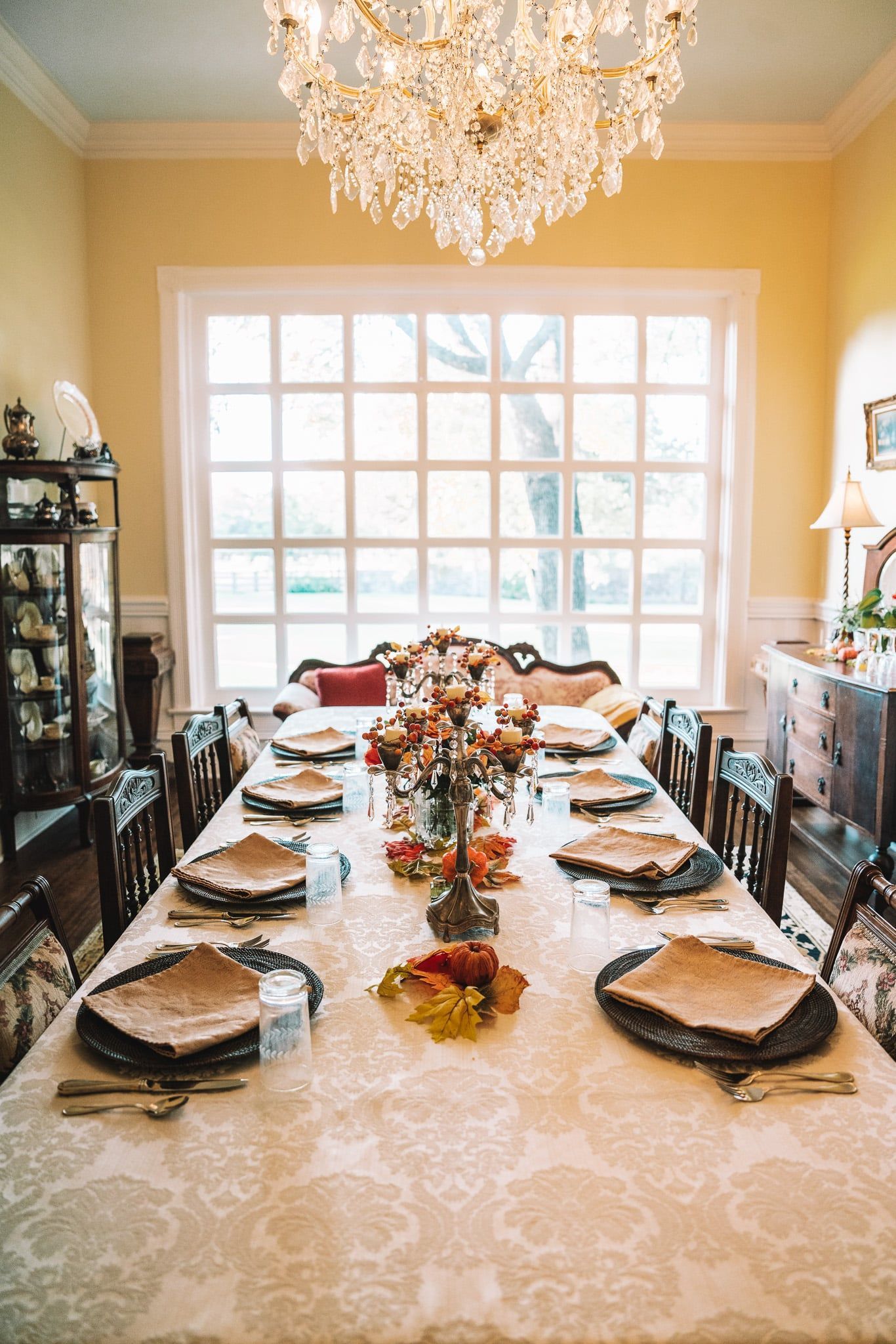 A long dining room table with plates , napkins , and a chandelier.