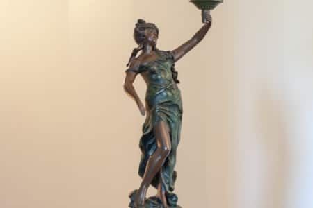 A bronze statue of a woman holding a candle in her hand.