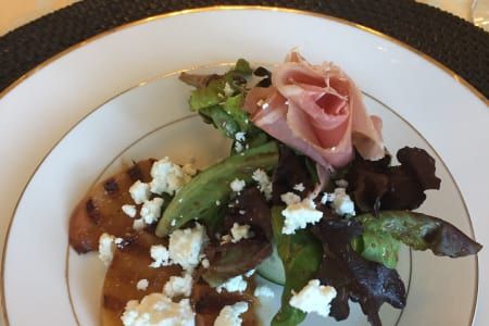 A white plate topped with a salad and ham on a table.