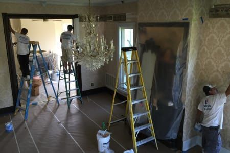 A group of people are painting a room with a chandelier.