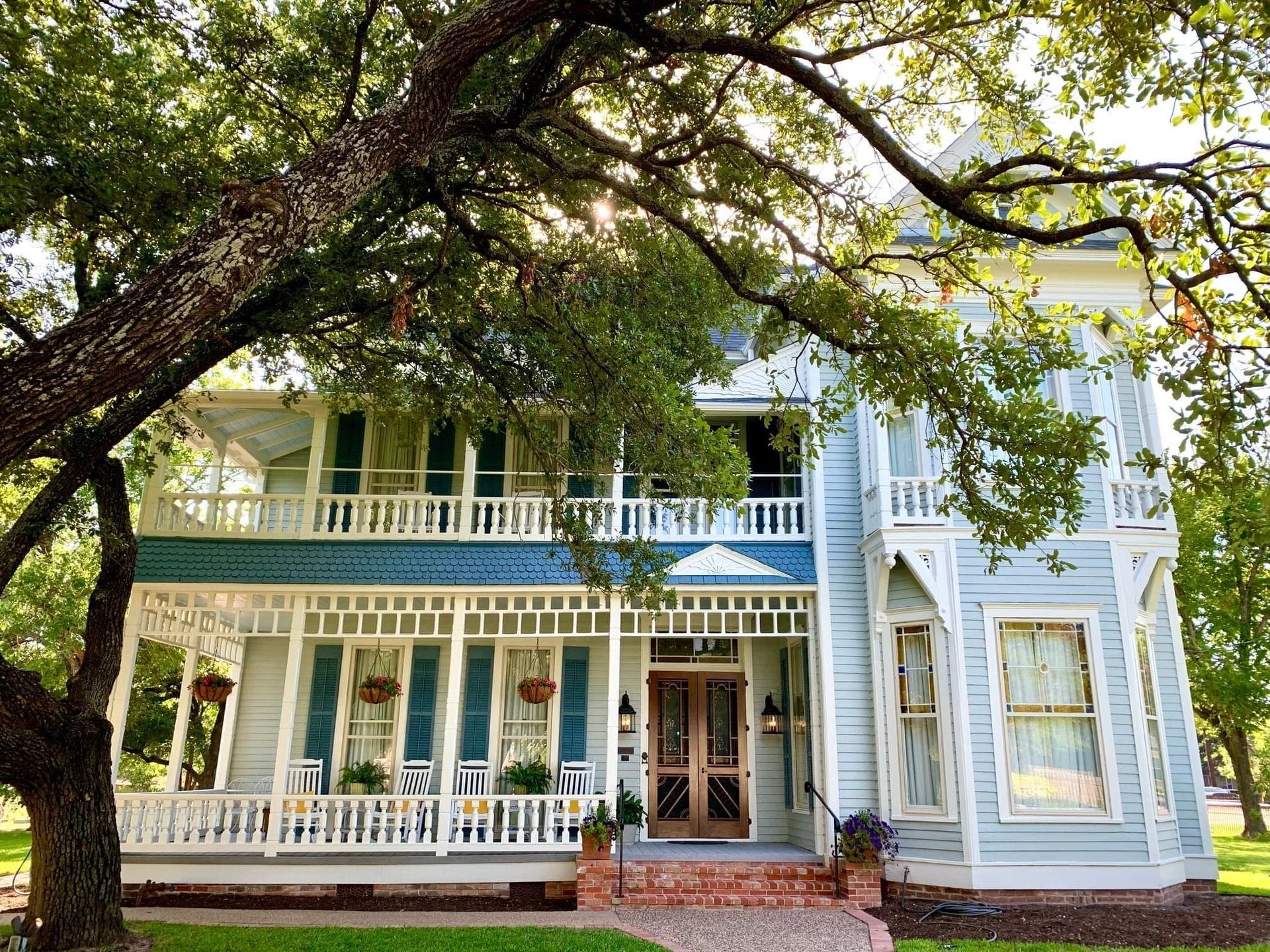 A large blue and white house with a large porch surrounded by trees.