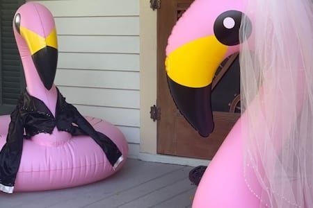 Two pink flamingos are sitting on a porch next to each other.