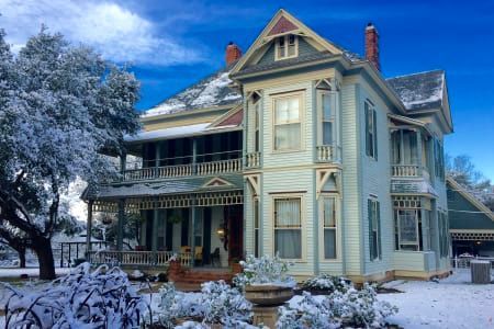 A large house with a large porch is covered in snow.