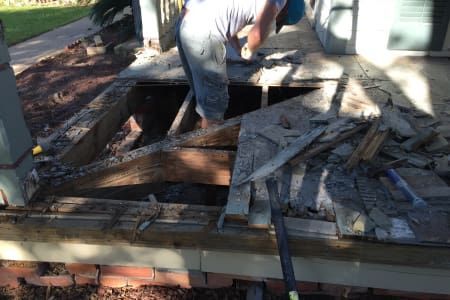 A man is working on a porch with a shovel.