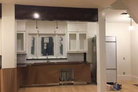 A kitchen under construction with white cabinets and a refrigerator.