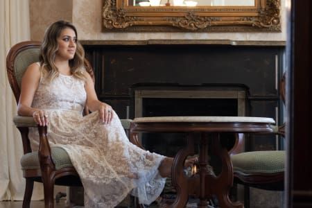 A woman in a white dress is sitting in a chair in front of a fireplace.