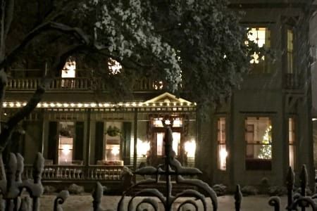 A large house is lit up at night with a wrought iron fence in front of it.