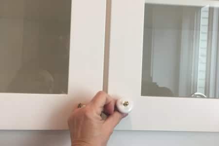 A person is opening a cabinet door with a white knob.