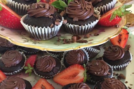A plate of chocolate cupcakes and strawberries on a table.