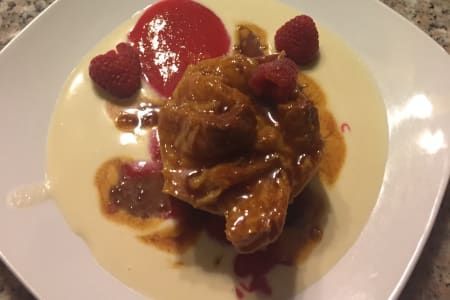 A white plate topped with a dessert with raspberries and sauce.