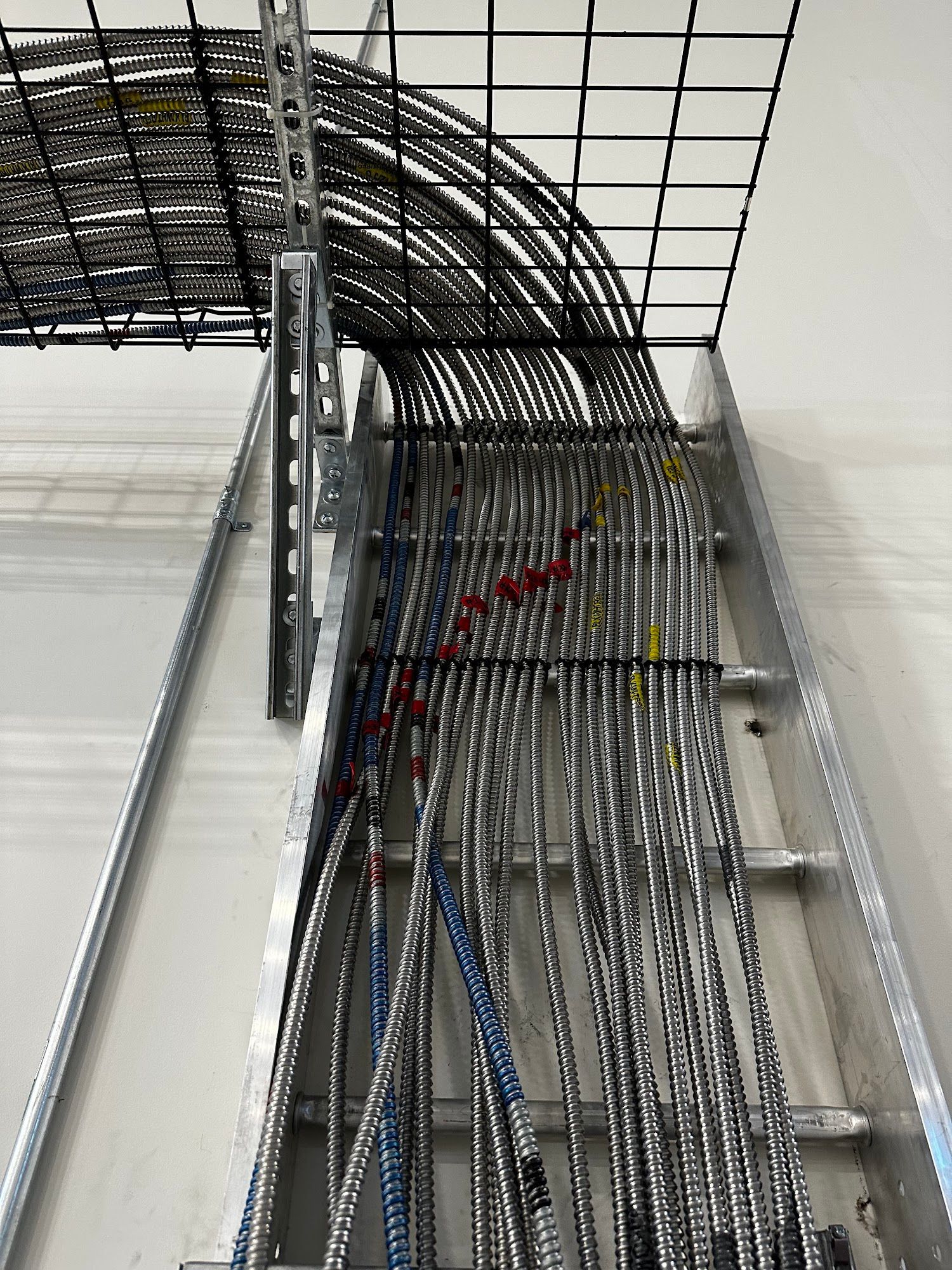 Cable bundles on a metal ladder and grid system, mounted on a white wall.